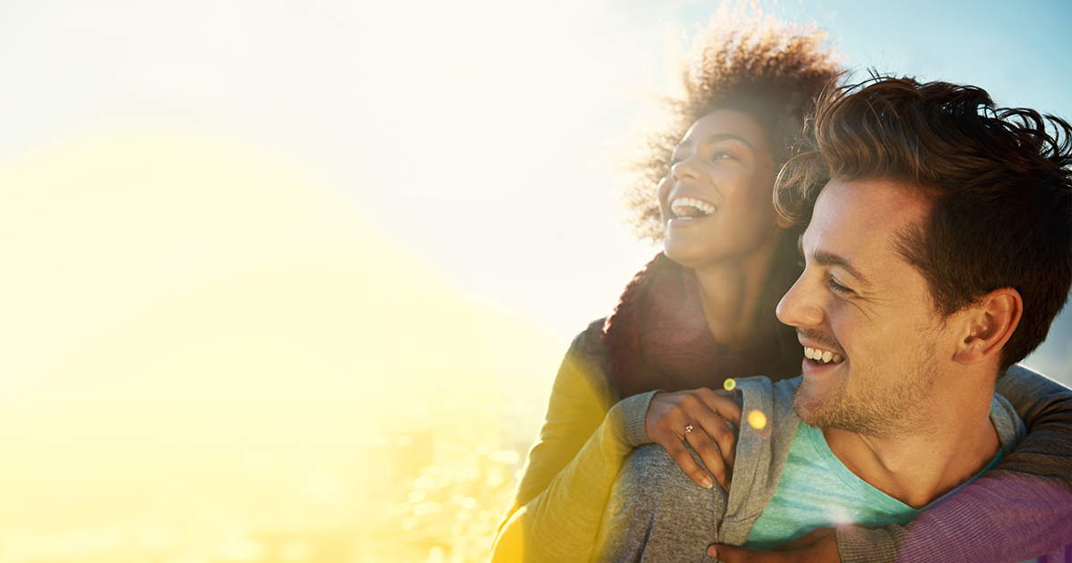 Couple smiling and embracing outdoors, sunlit.